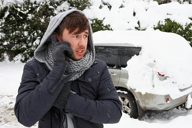 Young man in snow with broken down car on the phone