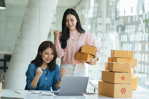 Two asian women with startup small business entrepreneur freelance working at home. checking product order. Online woman sellers working for e-business commerce. Shopping online, SME concept.