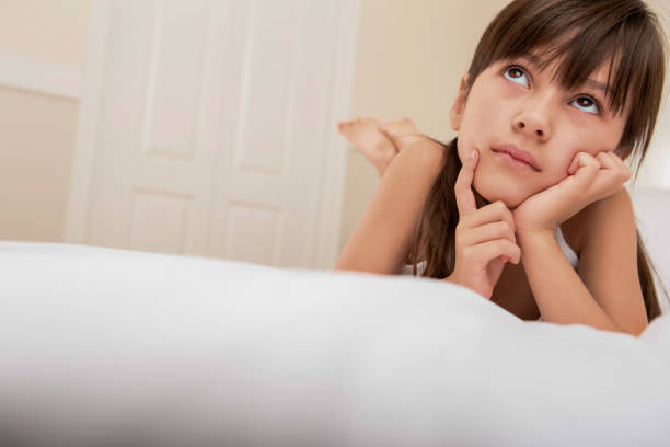 Pensive mixed race 7 years old girl laying on white bed