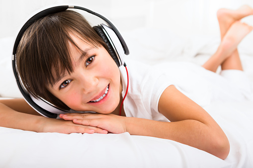 Happy 7 years old girl listening to headphone laying in bed