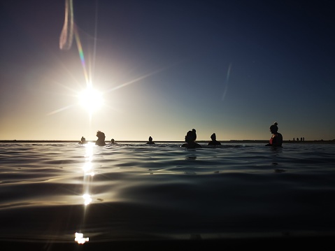 Burry Port, Wales, UK: January 13, 2022: A group of mature female friends swimming in the sea. Open or cold water swimming at sunset with silhouettes at surface level.