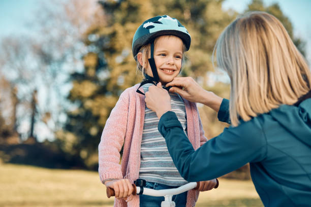 happy little girl enjoying while mother is adjusting her cycling helmet before the ride. - helmet bicycle little girls child imagens e fotografias de stock