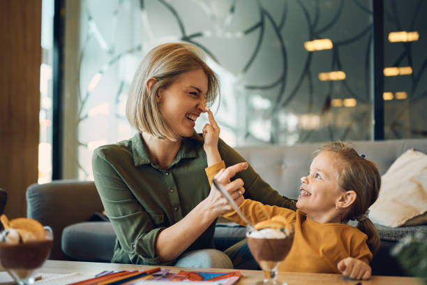 Playful mother and daughter having fun while eating mousse at home.