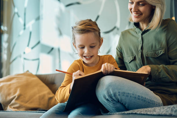 istock Smiling little girl sketching while spending a day with her mother at home. 1382829261