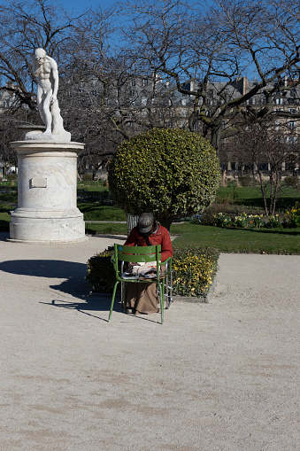 Juxtaposition of a local having breakfast and a statue, both looking down in Jardin des Tuileries near the Louvre, Paris, France.