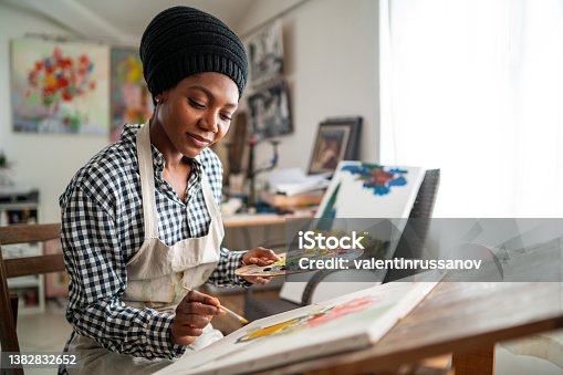 istock Afro female fine artist with traditional african hat 
 and apron, drawing in art studio 1382832652