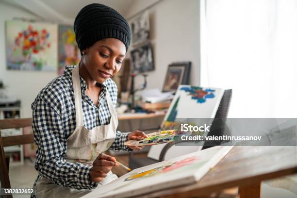 Afro Female Fine Artist With Traditional African Hat And Apron Drawing In Art Studio Stock Photo - Download Image Now