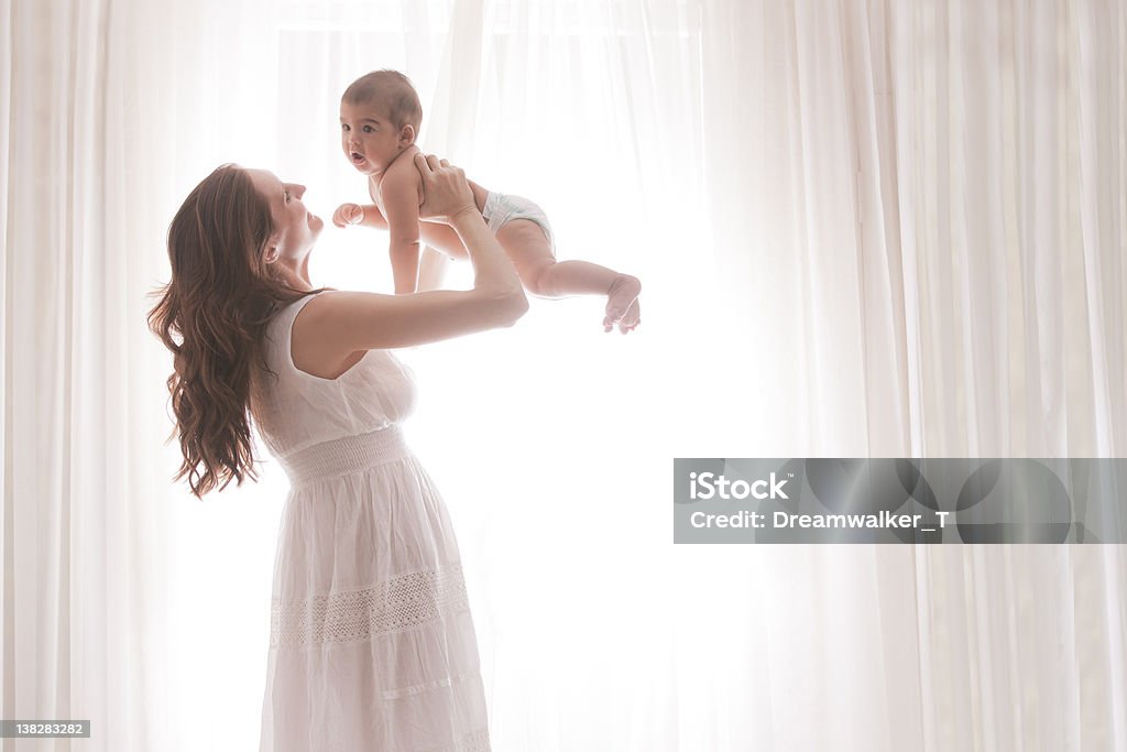 Mãe segurando o bebê filho por cortinas brancas - Foto de stock de Amor royalty-free