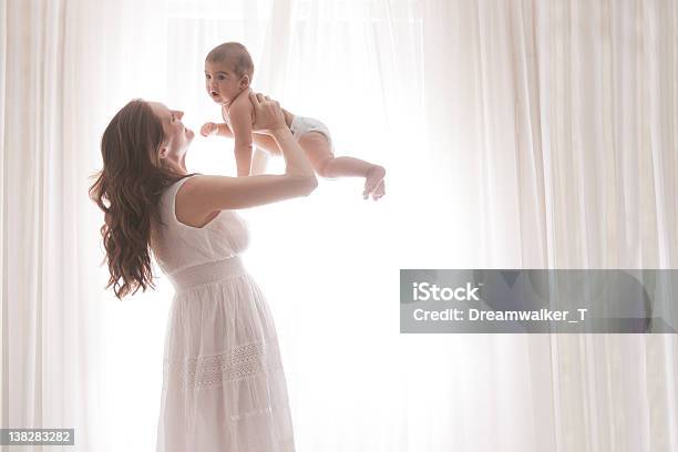 Foto de Mãe Segurando O Bebê Filho Por Cortinas Brancas e mais fotos de stock de Amor - Amor, Bebê, Branco