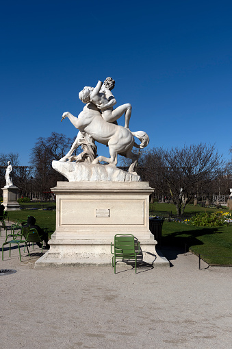 The centaur Nessus in Jardins de Tuileries, it was produced in 1892 and is in the gardens near the Louvre.  There is a man sat beside the sculpture. Paris, France, Europe.