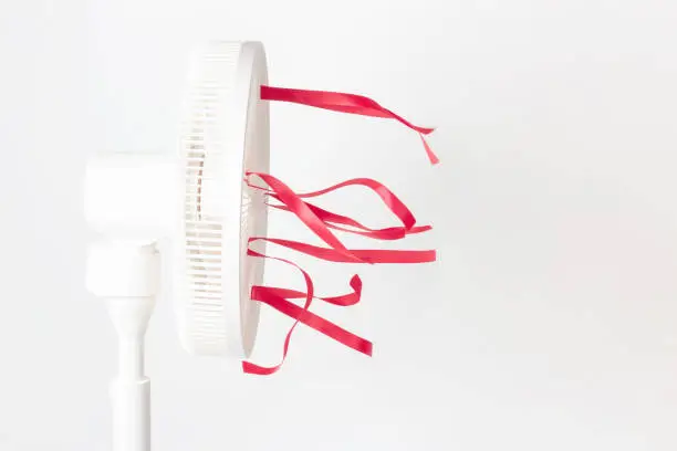 Photo of Electric fan with red ribbons on white background close-up, side view.