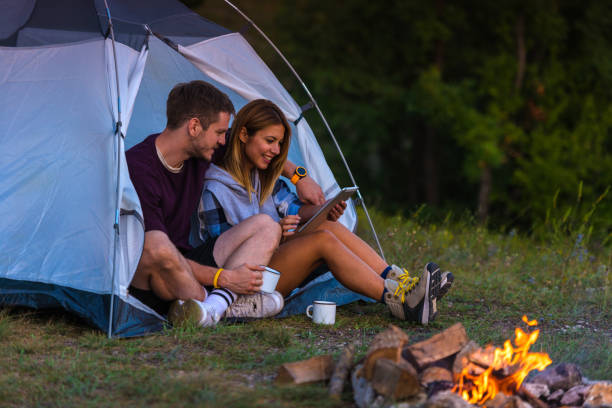 istock Young couple drinking coffee, enjoying the mountain view and checking the tablet with bonfire in the sunset 1382883643