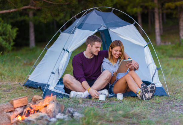 istock Young couple drinking coffee, enjoying the mountain view and checking the tablet with bonfire in the sunset 1382884794