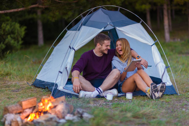 istock Young couple drinking coffee, enjoying the mountain view and checking the tablet with bonfire in the sunset 1382884797