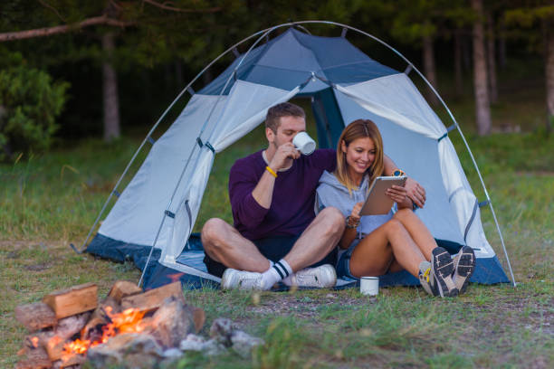 istock Young couple drinking coffee, enjoying the mountain view and checking the tablet with bonfire in the sunset 1382884801