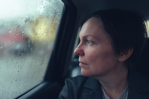 Businesswoman in taxi car looking out the window on a rainy day, selective focus