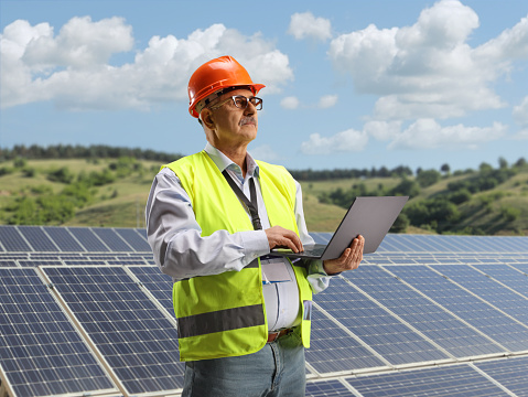 Mature male engineer working with a laptop on a photovoltaic solar panel field