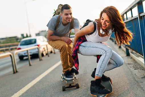 Portrait of happy couple having fun while driving a long board in city outdoors. People skateboard concept