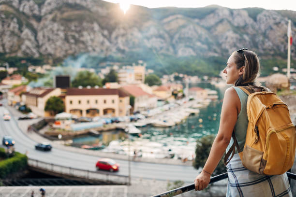 Millennial Caucasian woman with a backpack enjoys the view of the Adriatic Sea from the lookout. After reaching the lookout point from which the whole city can be seen, the female tourist paused for a moment to enjoy the view of the open sea and the natural beauty of Kotor. kotor montenegro stock pictures, royalty-free photos & images