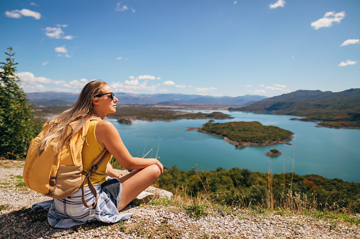 While hiking, the woman sat down to rest. She enjoys relaxing and looking at the beautiful alpine lake.