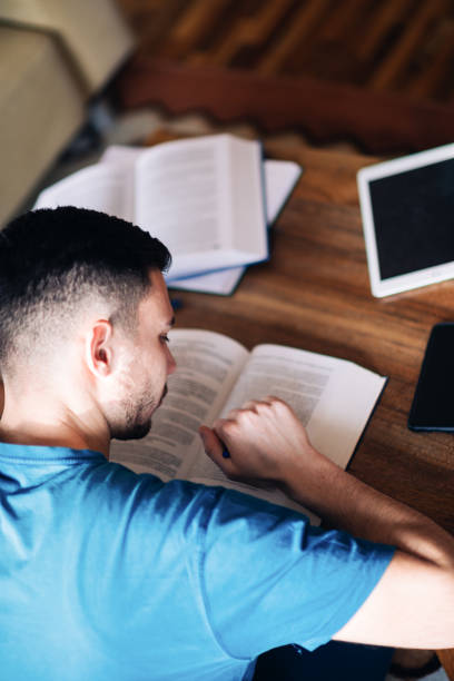 istock Handsome young man sitting on a sofa at home reading a hardcover book 1382912895