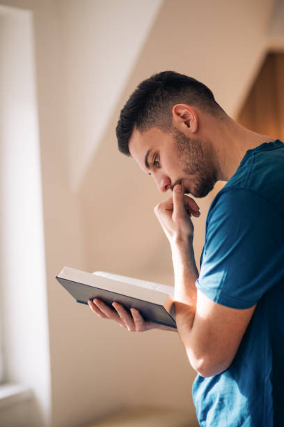 istock Student reading a book while standing and walking in the room next to the windows. 1382914114