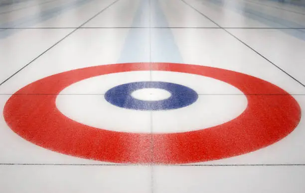 An empty house from the sport curling on a sheet of ice in a curling arena. *NOTE* that the ice is NOT smooth and has a rough, uneven texture. Focus is on button, or middle of the house.