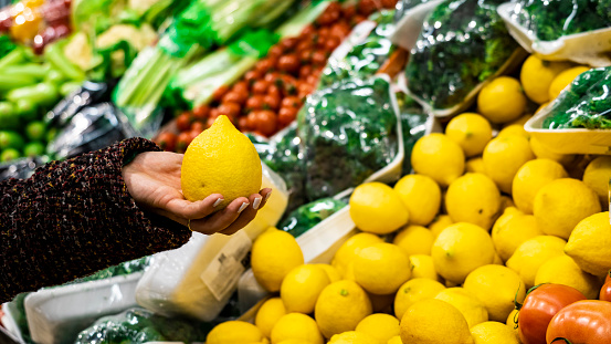 Woman holding a lemon in the vegetable aisle at the market