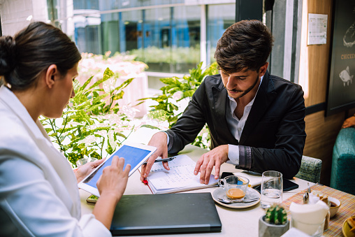 Portrait of young business man and woman sitting in café and discussing contract