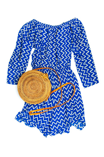 Stylish trendy feminine summer clothing blue dress jumpsuit, round rattan bag on white background Trendy hipster look Female fashion background blog concept Flat lay top view.