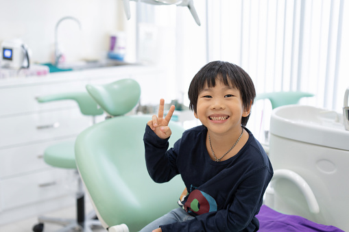 El chico asiático se siente feliz de sentarse en la silla dental en la clínica dental photo