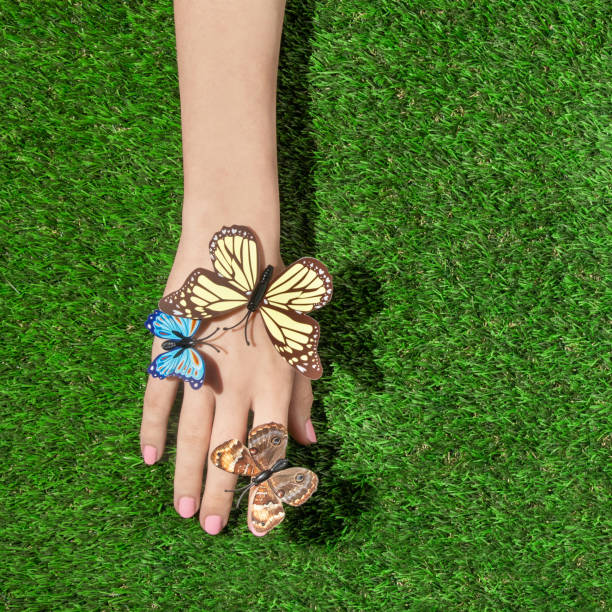 istock Spring creative layout with colorful butterflies on hand against bright green grass background. Romantic fashion aesthetic concept. Minimal summer idea. 1382985727