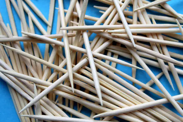 Photo of A pile of wooden toothpicks lie on a blue background.
