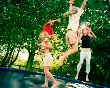 Boys jumping on trampoline at backyard with water sprayer. Summer fun. Simple living.