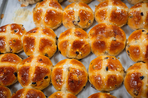 Close up color image depicting a collection of freshly baked hot cross buns - an easter culinary tradition, especially in the UK - in a row. Room for copy space.