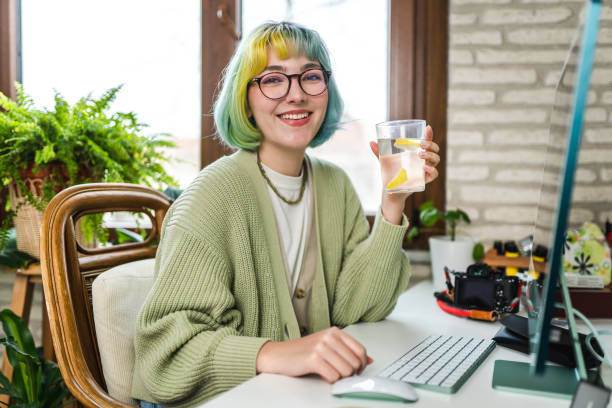 giovane donna che beve acqua mentre lavora - foods and drinks simplicity purity clothing foto e immagini stock