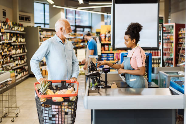 mitarbeiter im supermarkt bedient senior-kunden mit gesichtsmaske - kassiererin supermarkt stock-fotos und bilder