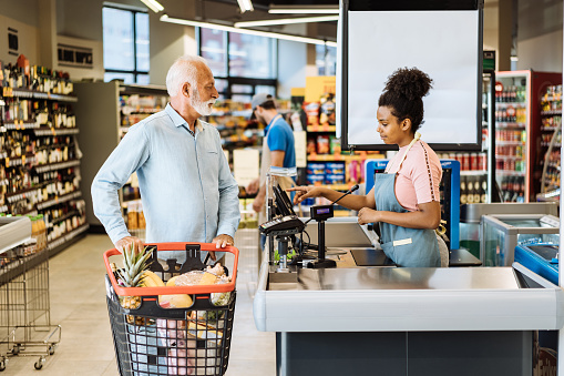 Employee in supermarket serving senior customer with face mask