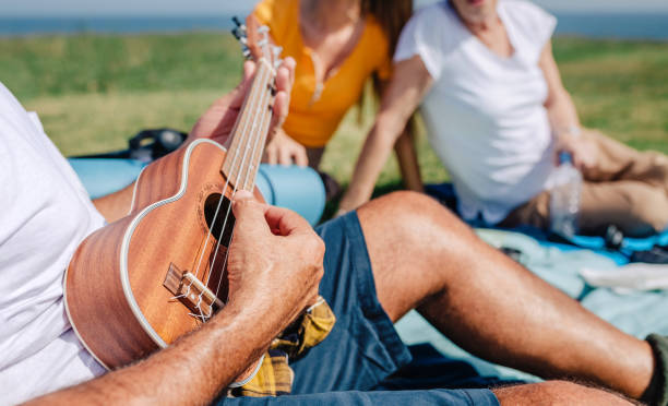 istock Senior man playing ukulele for his family sitting on a blanket during an excursion 1383006801