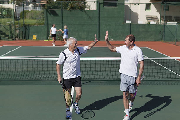 пожилые мужчины высокого fiving на теннисный корт - doubles стоковые фото и изображения