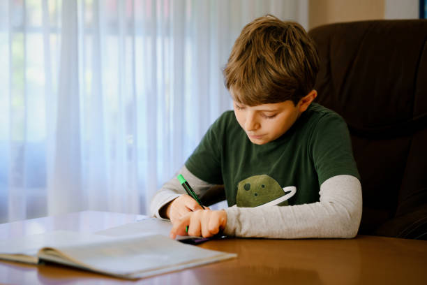 istock Hard-working happy school kid boy making homework during quarantine time from corona pandemic disease. Healthy child writing with pen, staying at home. Homeschooling concept 1383008442