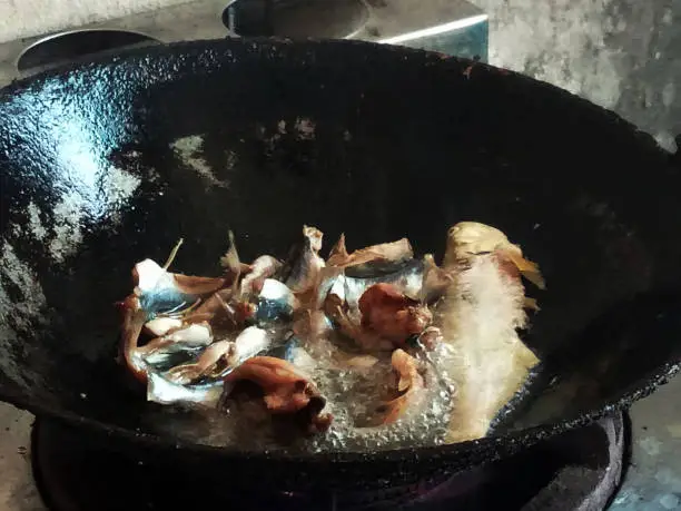 Fried sun dried salted seafish with boiled oil in iron pan in kitchen room of countryside rural house at Phatthalung city inn Phatthalung, Thailand