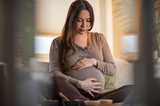 Pregnant woman feeling pain while sitting in living room stock photo