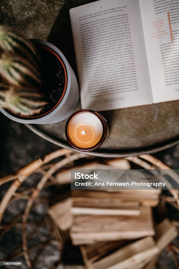 cozy cabin getaway weekend open book on grey round table with burning candle, cactus plant Candle Stock Photo