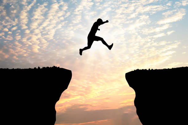 istock Silhouette young man jumping over precipice between two rocky mountains at sunset. 1383016841