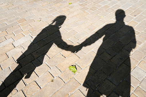 Shadow of man and little girl on stone pavement holding hands with green leaf on floor. Anonymous parent, natural bonding concepts