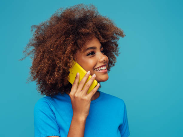 hermosa chica sonriente con peinado rizado usando un teléfono inteligente - fashion isolated objects beauty and health clothing fotografías e imágenes de stock