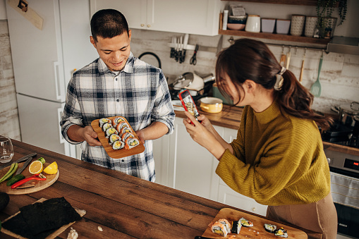 Two people, modern Japanese couple prepared sushi together in kitchen at home. Woman is photographing their lunch.