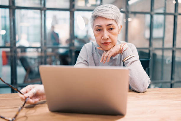 riflessiva confusa matura donna d'affari asiatica preoccupata pensando al problema online guardando il computer portatile, preoccupata donna di mezza età senior che legge cattive notizie di posta elettronica. - professional occupation firing people adversity foto e immagini stock