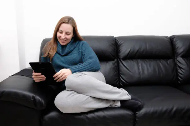 Woman sitting on sofa using tablet to watch funny video